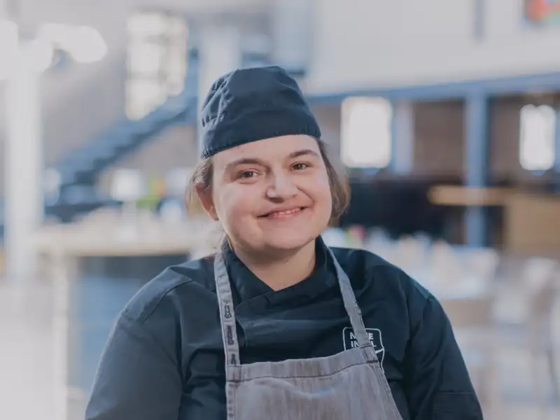 Eine junge Frau in Arbeitskleidung lächelt in die Kamera