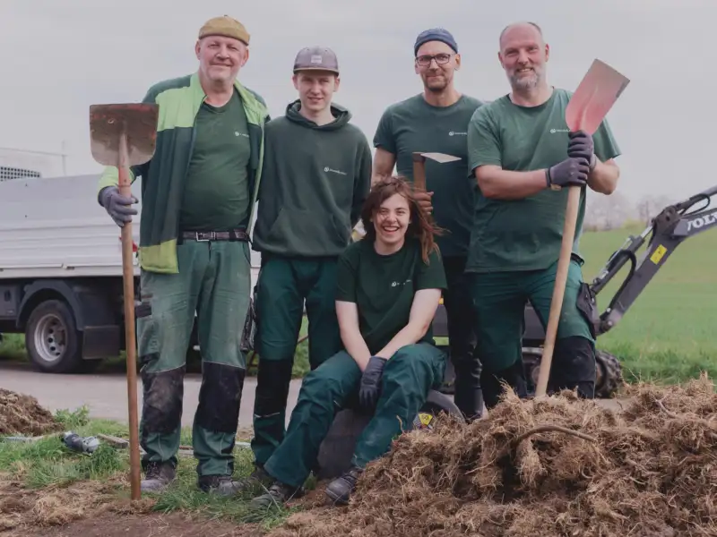 Fünf Menschen mit und ohne Behinderung in Garten-Arbeitskleidung mit Schaufeln in der Hand.