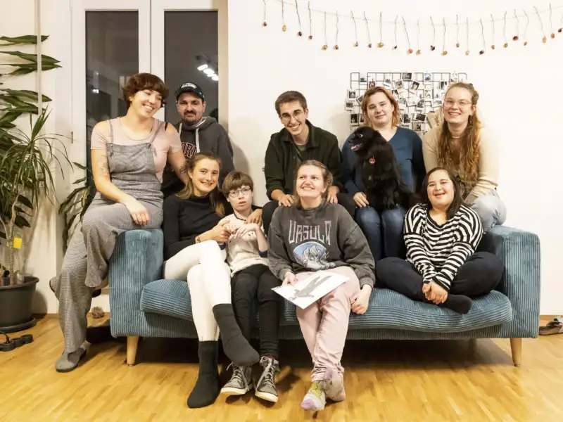 Eine Gruppe von Menschen mit und ohne Behinderung sitzt gemeinsam auf einem Sofa