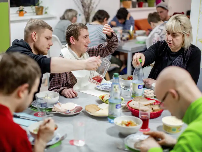 Frauen und Männern mit und ohne Behinderung sitzen beim gemeinsamen Essen am Tisch.
