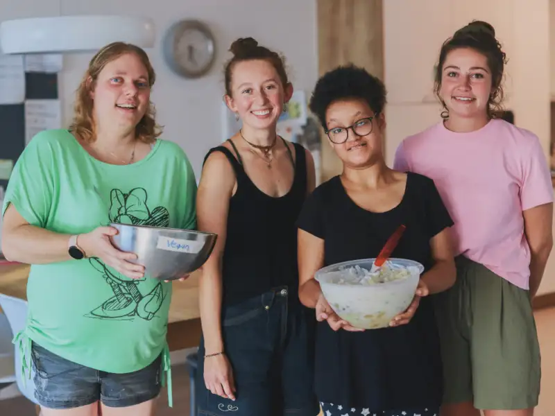 Vier junge Frauen in der Küche, zwei tragen Schüsseln in den Händen.