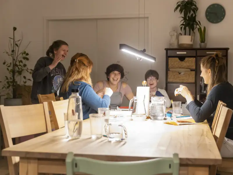 Fünf junge Frauen lachen an einem großen Tisch.