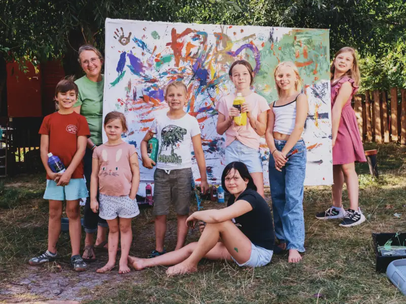 Eine Gruppe von Kindern in der Natur vor einem bunt bemalten Bild.