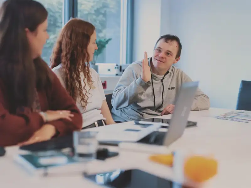 Eine Gruppe junger Menschen sitzt an einem Tisch und unterhält sich. Vor ihnen steht ein Laptop.