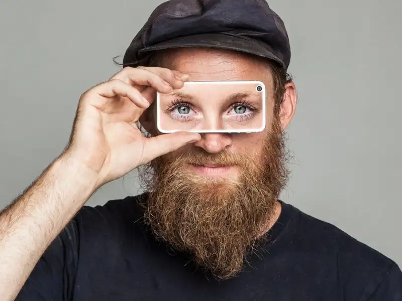 Ein mann hält sich ein Handy vor die Augen. Seine Augenpartie ist durch das Handy zu sehen.