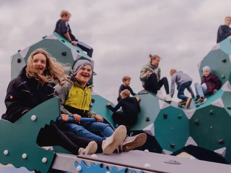 Besucher des inklusiven barrierefreien Spielplatzes im Mehrgenerationenpark in Timmel testen die Wippe und (im Hintergrund) das neue Klettergerüst.