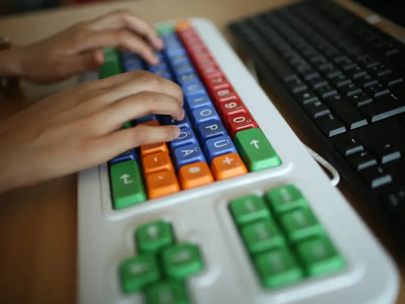 Zwei Hände sind auf einer bunten Computertastatur zu sehen.