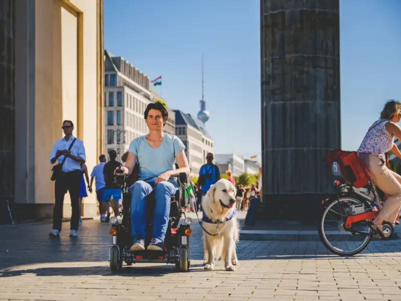 Barrierefreiheit und Tourismus in Berlin. Eine frau im Rollstuhl vor dem Brandenburger Tor.