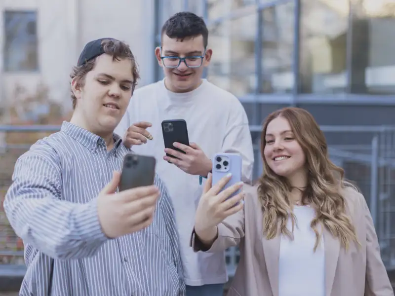 Drei junge Menschen schauen interessiert auf ihre Smartphones.