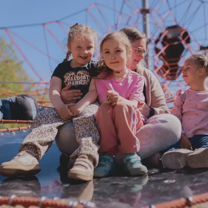 Aktion Mensch - 30.4.2026 - Kinder spielen, klettern und toben auf dem Spielplatz Stück zum Glück Rheda-Wiedenbrück. Heut sind die Kinder der Kita Tausendfüssler mit ihrem Kita-Leiter Konrad Vielstädte im Flora-Park in Rheda-Wiedenbrück. Teilnehmerin Finja ist 5 und würde am liebsten den ganzen Tag klettern, rennen und rutschen. Heute kann sie genau das machen. Mit ihrer inklusiven Kita besucht sie den neuen barrierefreien Spielplatz. Hier können wirklich alle Kinder zusammen toben und Spaß haben. Eine Kindergärtnerin der inklusiven Kita Tausendfüssler in Rheda-Wiedenbrück (Mitte hinten) mit drei Kindergartenkindern auf einem Klettergerüst des neuen barrierefreien Spielplatzes im Flora-Park in Rheda-Wiedenbrück.