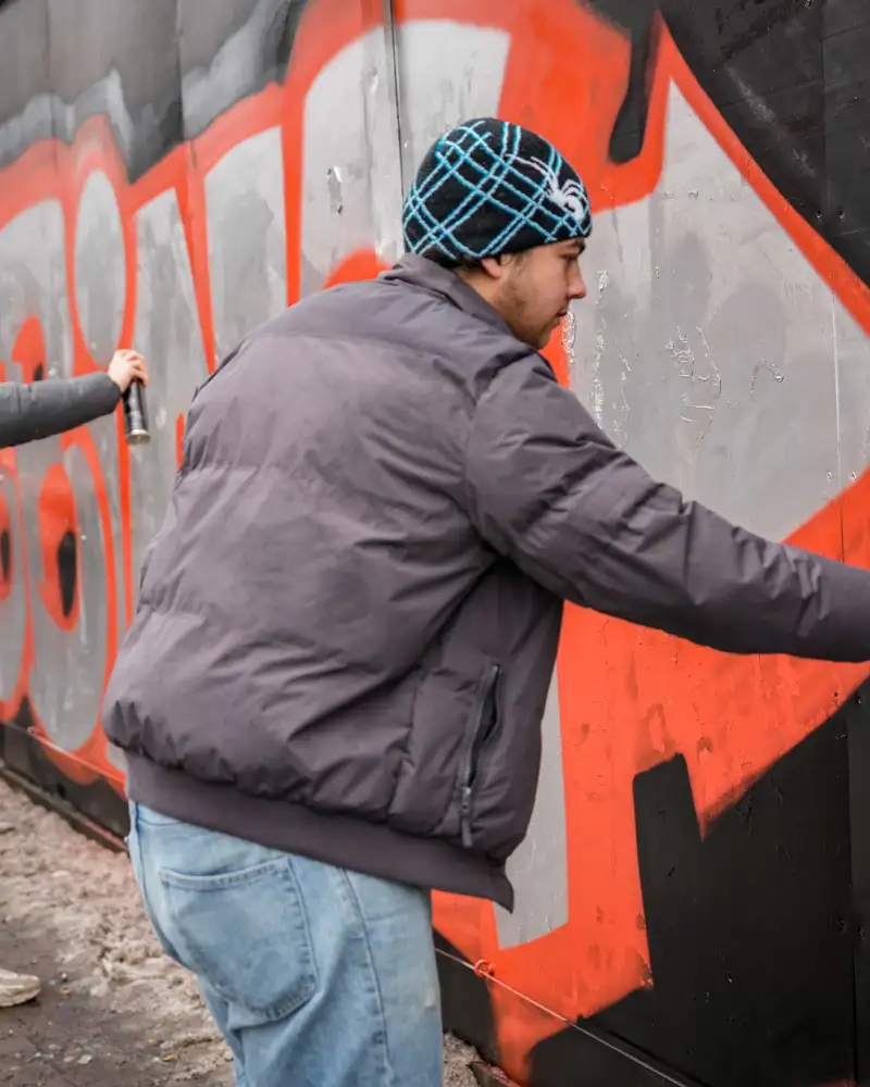 Vor einer mit bunten Graffitis besprühten Wand stehen einige Jugendliche. Sie sind dabei, ein neues Bild an die Wand zu malen.