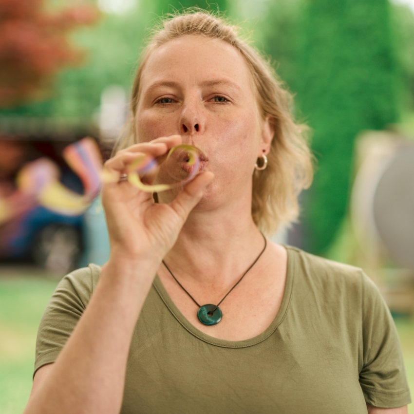 Gewinnerin Claudia - eine Frau mit mittellangen, blonden Haaren - steht in einem Garten und pustet eine Luftschlange.