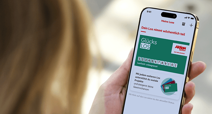 Auf einem Mobiltelefon ist die App der Aktion Mensch geöffnet. Darin ist das grüne Glücks-Los der Aktion Mensch zu sehen.