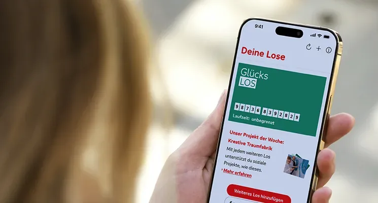Auf einem Mobiltelefon ist die App der Aktion Mensch geöffnet. Darin ist das grüne Glücks-Los der Aktion Mensch zu sehen.