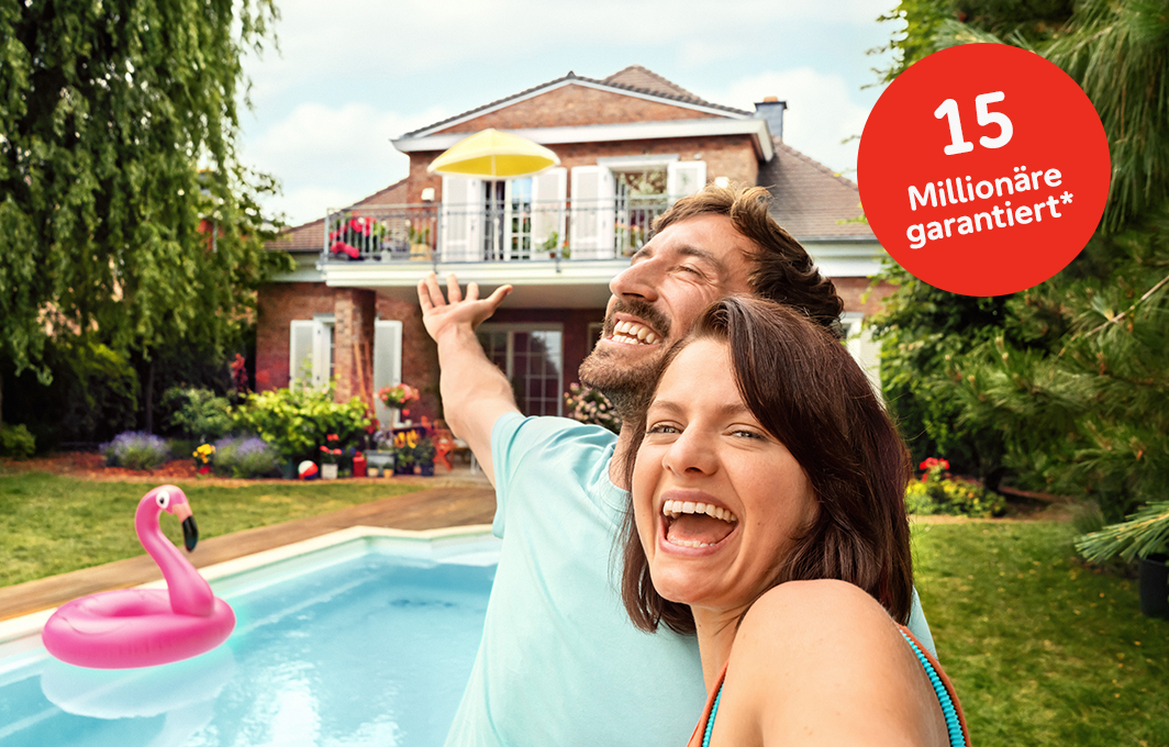 Ein Paar macht ein Selfie und zeigt auf ihr Traumhaus im Hintergrund.
