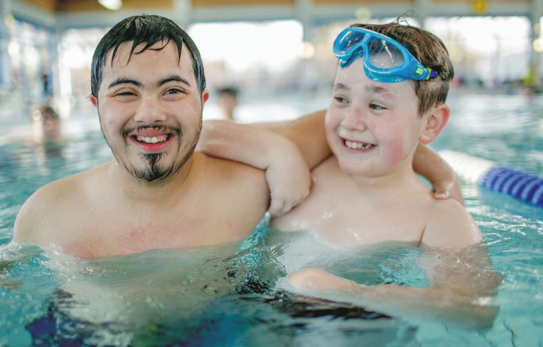 Zwei Jungen sind im Schwimmbad und haben lachend die Arme umeinander gelegt.
