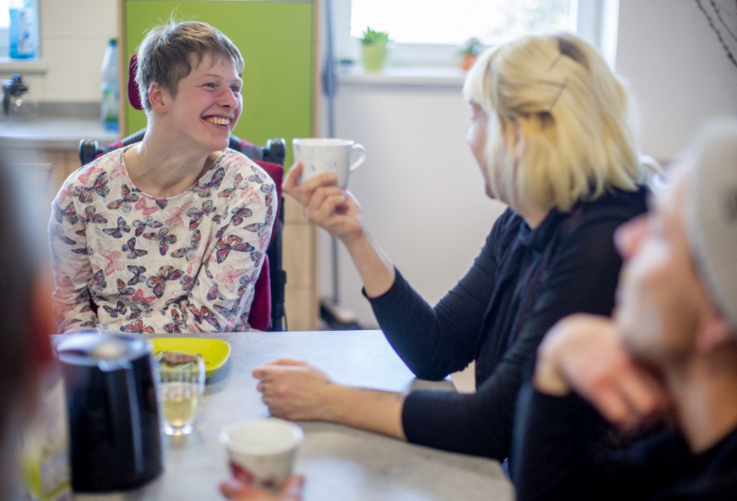 Eine Frau mit Behinderung und eine weiter Frau sitzen am Tisch und frühstücken.