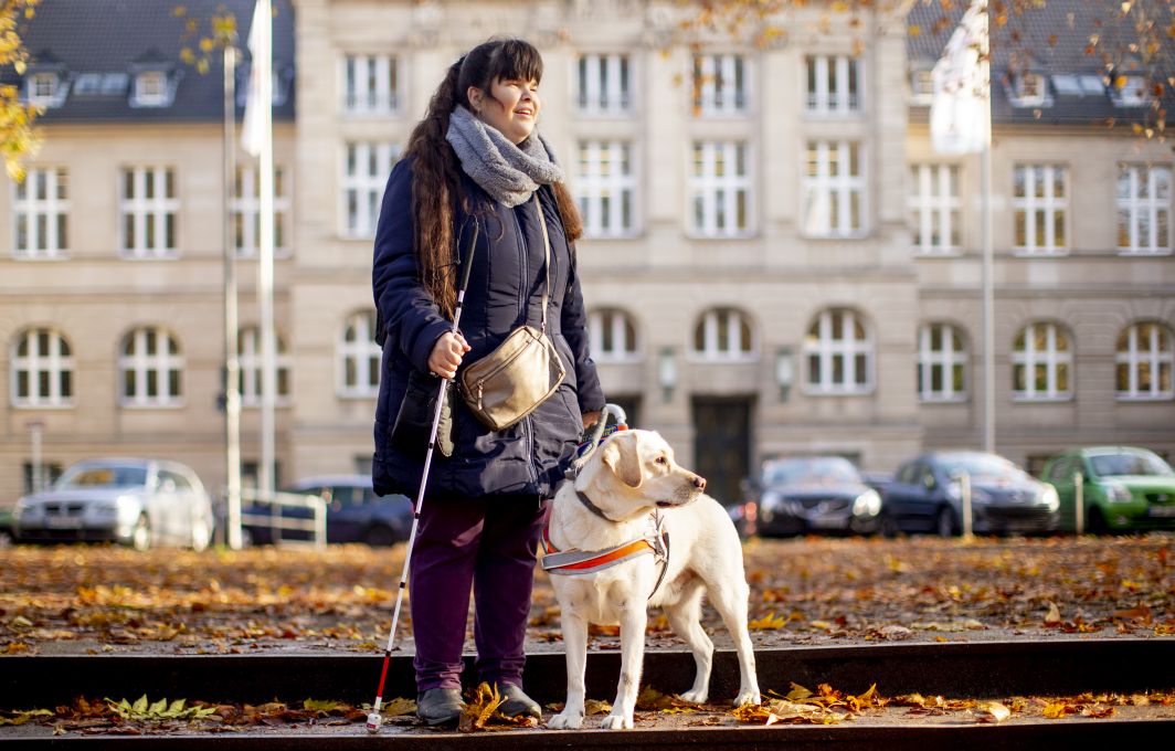 Eine junge Frau und ihr Blindenführhund Pitou stehen vor dem Universitäts-Gebäude.