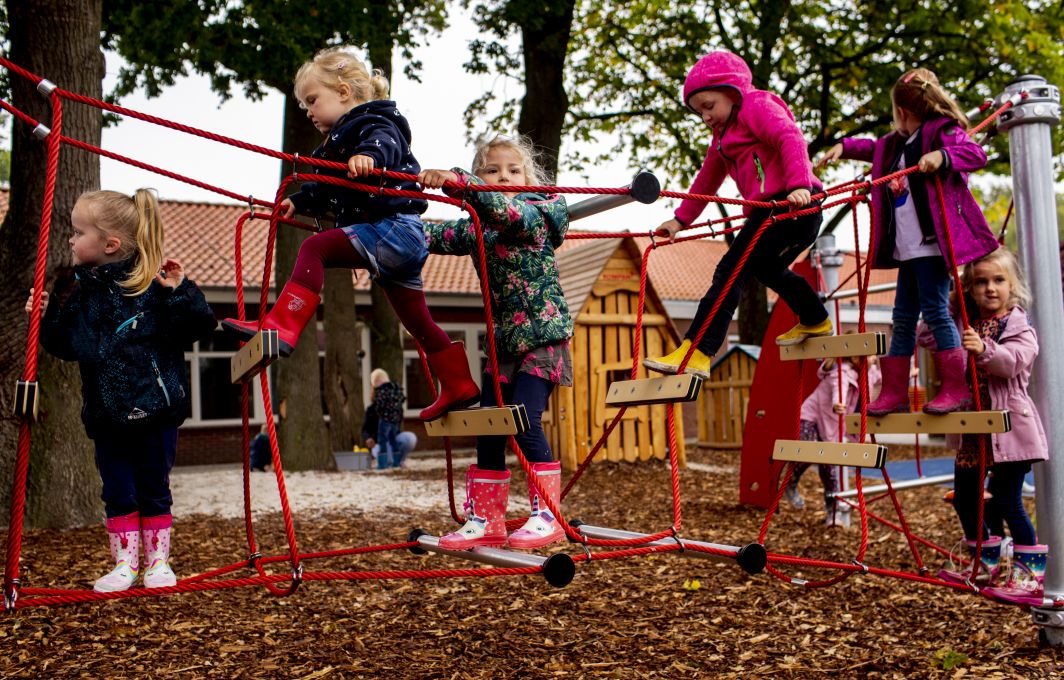 Kinder laufen über eine Hängebrücke auf dem Spielplatz.