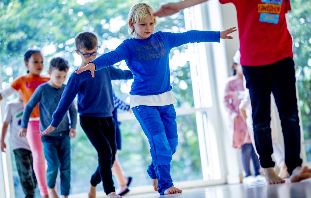 Kinder balancieren in einer Turnhalle über ein imaginäres Seil.