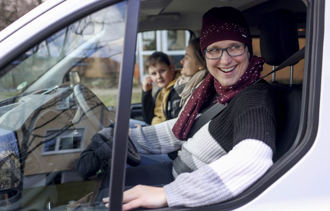 Melanie Grochalsky sitzt auf der Fahrseite im Kleinbus und lacht in die Kamera.