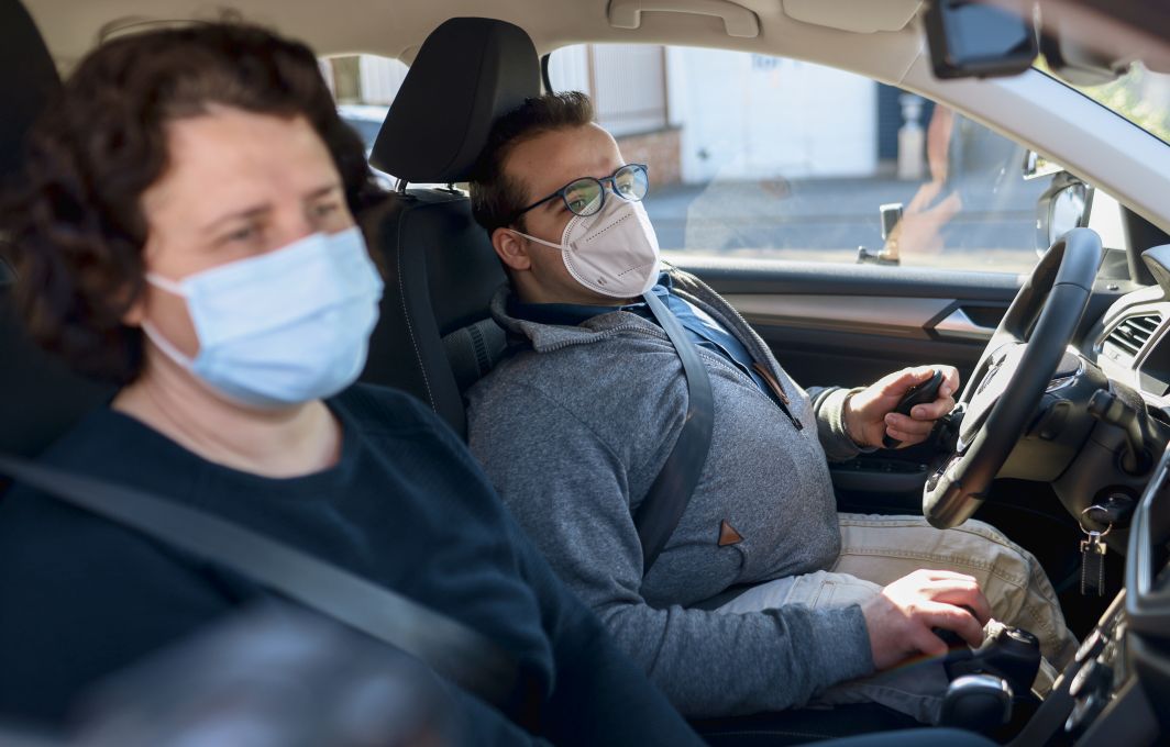 Ein Mann mit Behinderung sitzt am Steuer eines Autos. Auf dem Beifahrersitz ist die Fahrlehrerein.