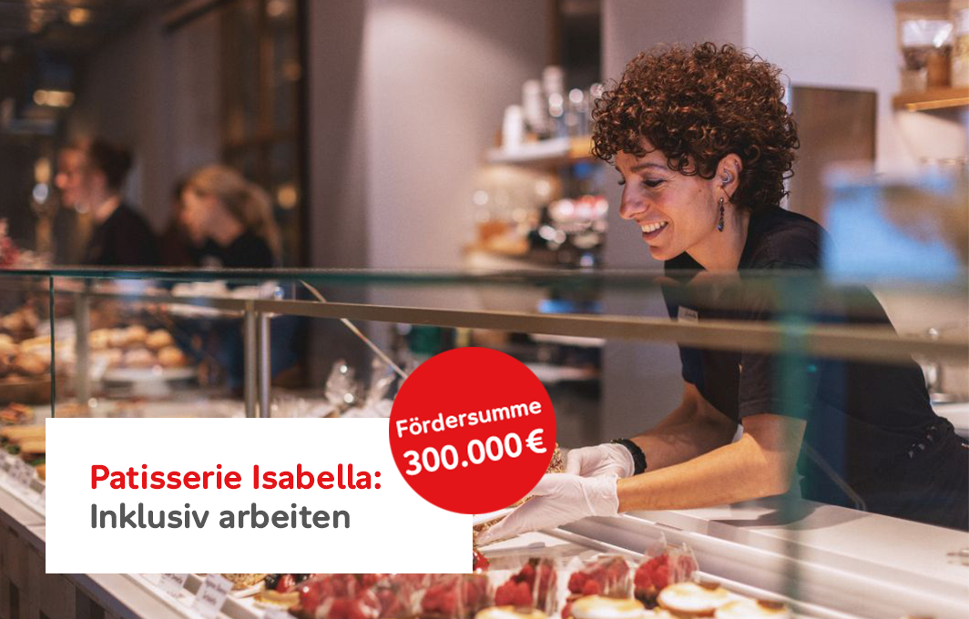 Eine Frau mit Hörgerät steht hinter einer Kuchentheke und stellt ein Blech mit Kuchen in die Vitrine. Aufschrift: "Patisserie Isabell: Inklusiv Arbeiten. Fördersumme: 300.000 Euro."