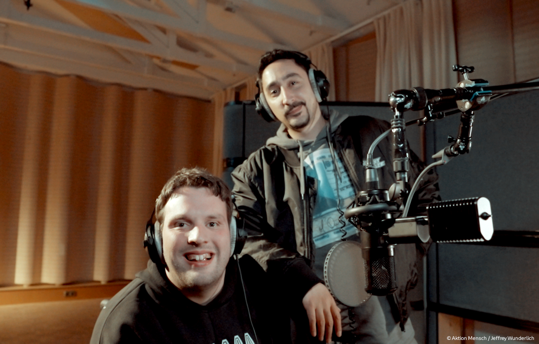 Eko Fresh und Rolling G sind im Tonstudio. Rechts im Bild ist ein Mikrofon zu sehen. Rolling G sitzt im Rollstuhl, Eko Fresh lehnt sich auf seine Schulter.