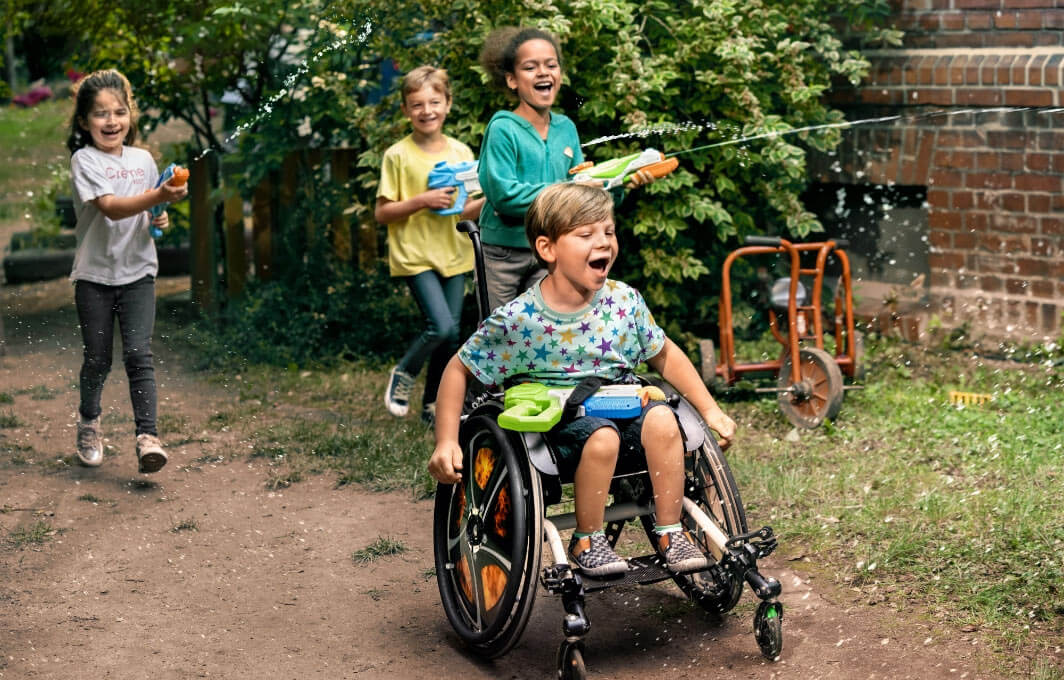 Kinder spielen gemeinsam. Ein Kind sitzt im Rollstuhl.