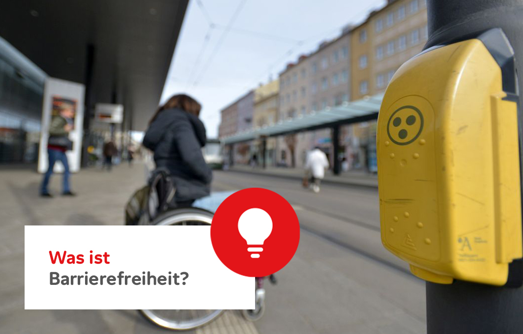 Rechts im Bild ist eine Blindenampel fokussiert. Im Hintergrund sieht man unscharf eine Person im Rollstuhl, die an der Straße wartet. Schriftzug: "Was ist Barrierefreiheit?"