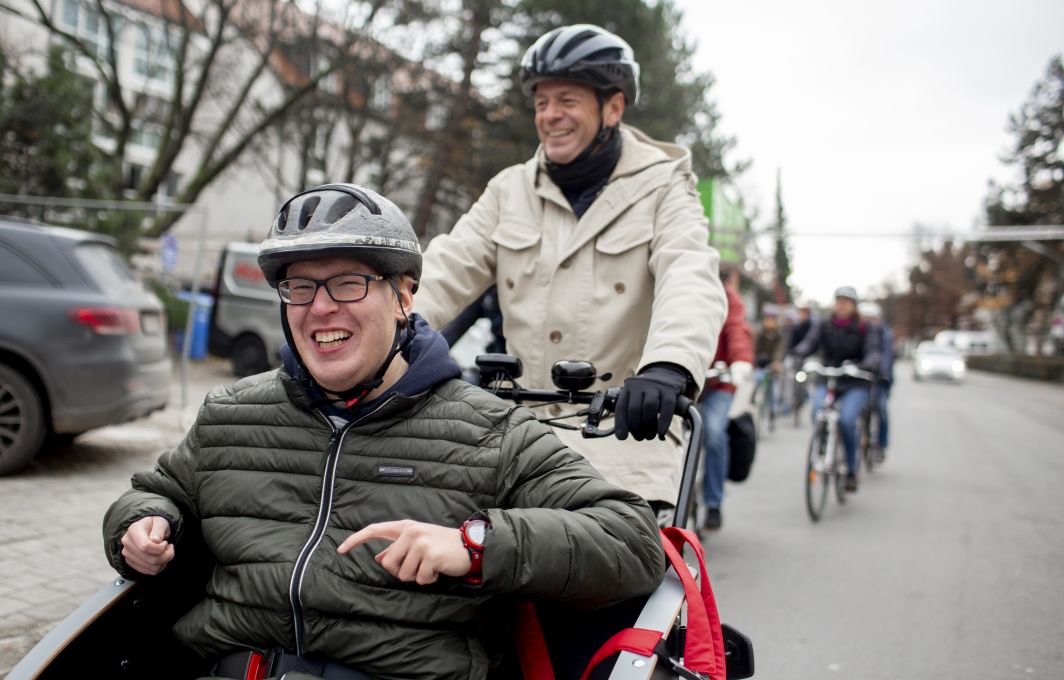Rudi Cerne fährt einen jungen Mann in der Fahrrad-Rikscha. Der Mann freut sich.