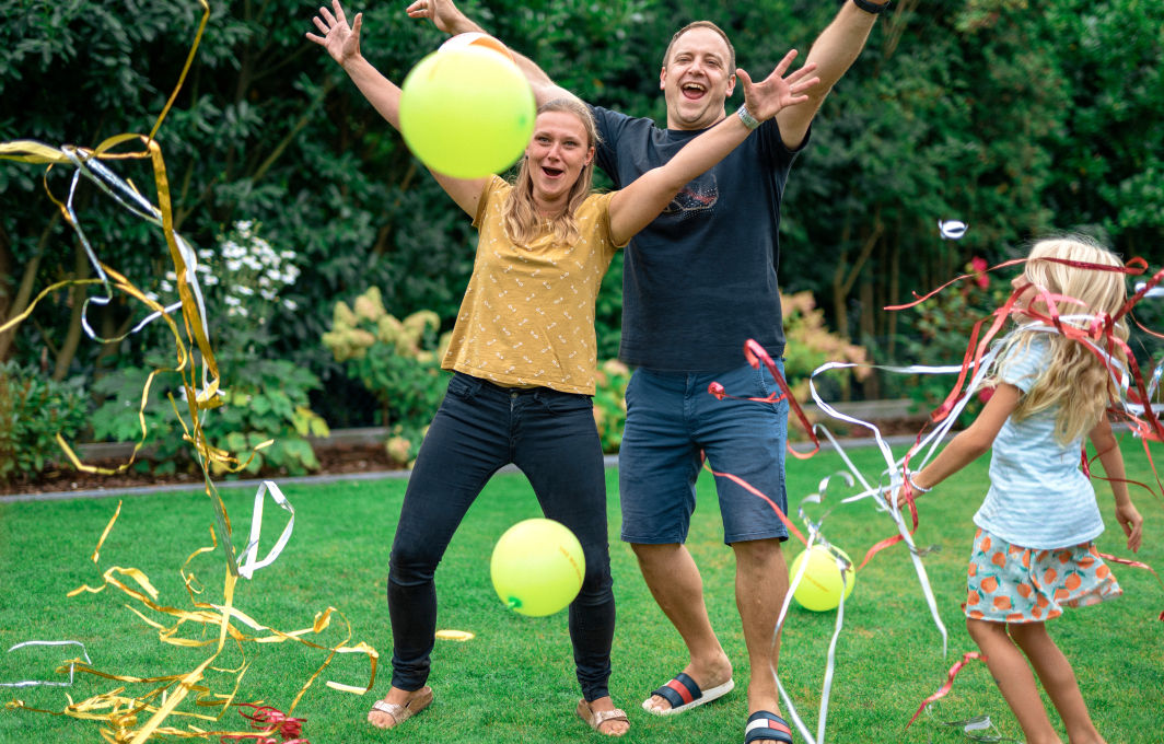 Eine Familie jubelt. Luftschlangen und Ballons fliegen durch das Bild.
