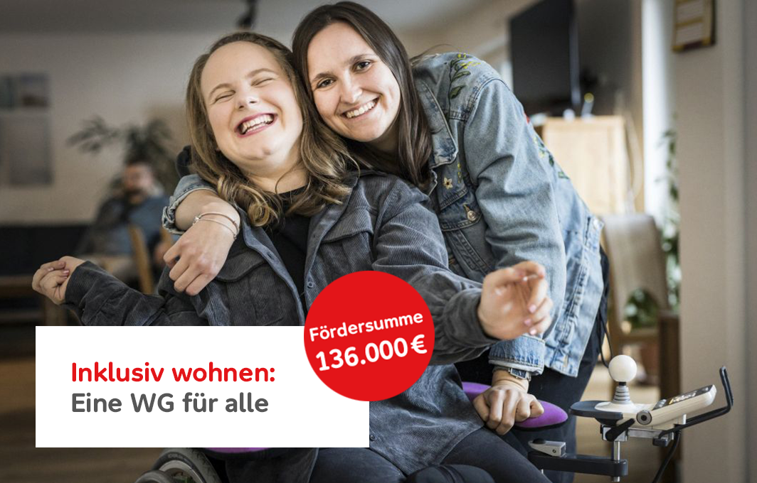 Luisa sitzt im Rollstuhl und lacht. Eine Mitbewohnerin legt von hinten den Arm um sie und lacht auch in die Kamera.