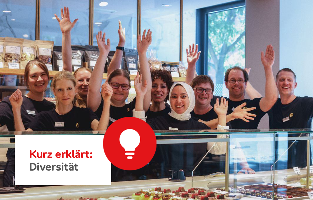Eine Gruppe von Frauen und Männern steht hinter der Theke eine Konditorei. Einige der Menschen haben eine Behinderung, eine Frau trägt ein Kopftuch. Infobox unten links: Kurz erklärt: Diversität