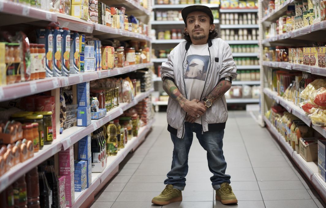 Gia steht im Supermarkt und schaut ernst in die Kamera.