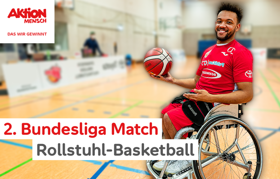 Leeroy sitzt im Rollstuhl und hält lachend einen Basketball hoch.