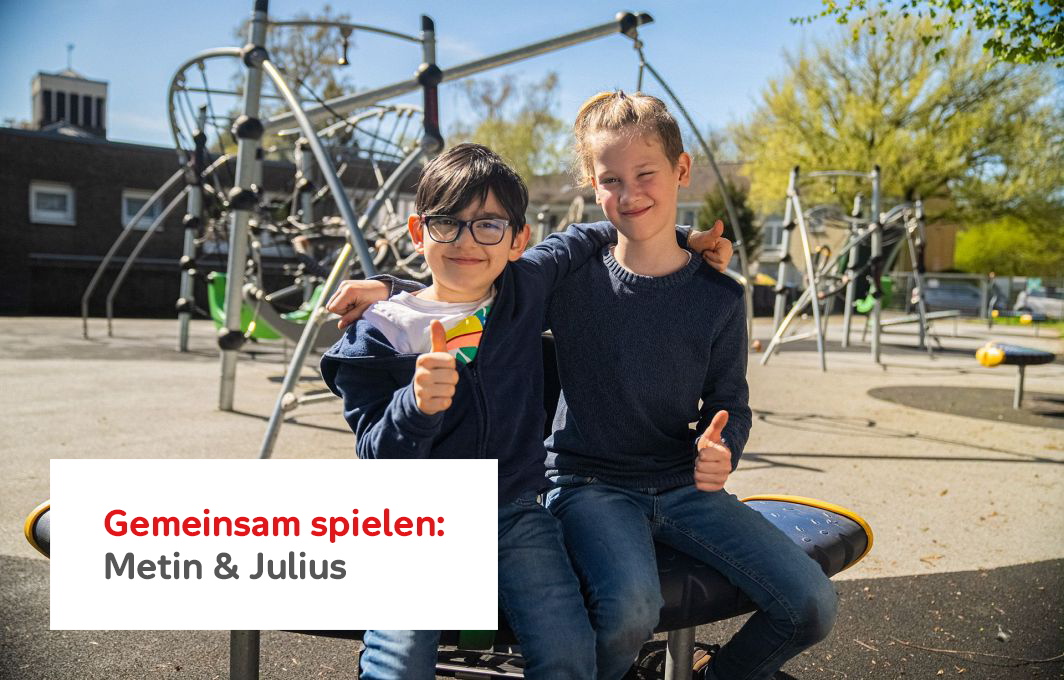 Metin und sein Freund Julius sitzen auf einem Spielgerät. Sie haben die Arme umeinander gelegt und zeigen Daumen hoch in die Kamera.