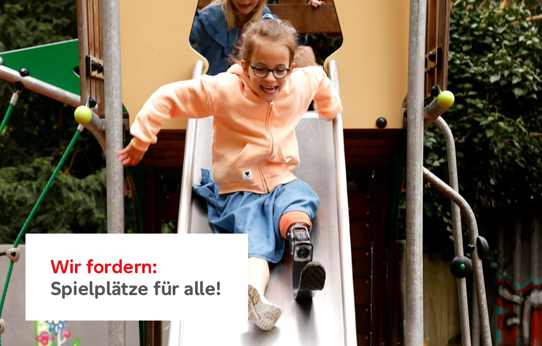 Ein Mädchen mit einer Beinprothese rutscht lachend eine Rutsche hinunter.