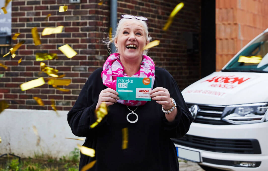 Unsere Gewinnerin Tina hält ihr Glücks-Los in die Kamera und freut sich. Von oben regnet Konfetti auf sie.