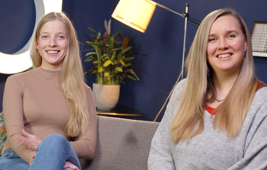 Cindy und Fabie sitzen auf einer Couch und lachen in die Kamera.