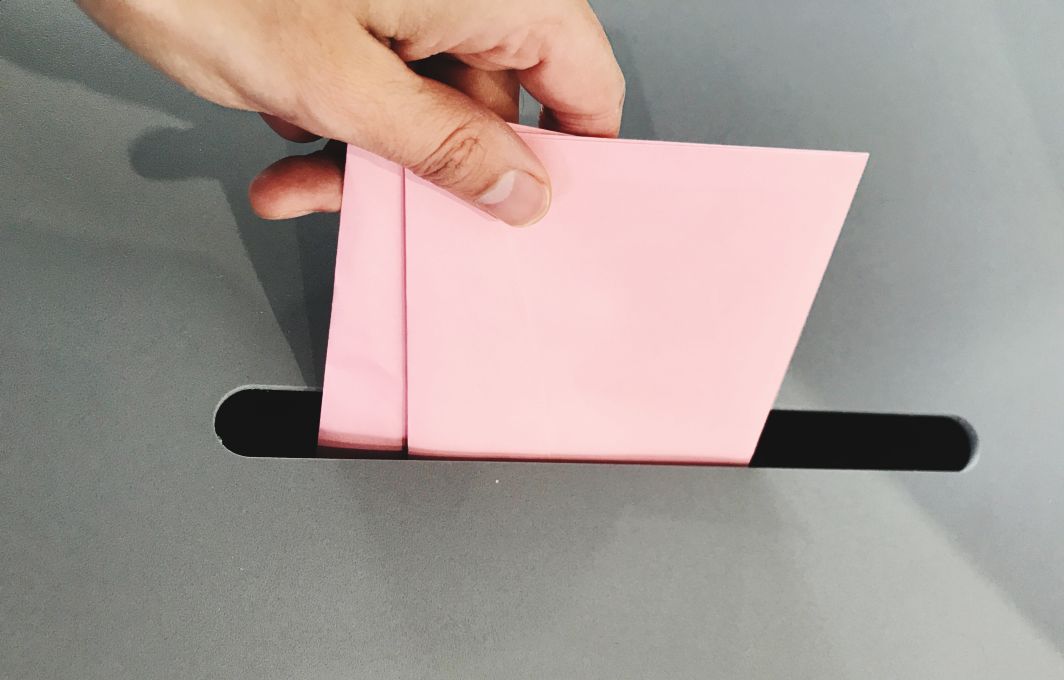 EIne Hand wirft einen rosafarbenen Umschlag in eine Wahlurne