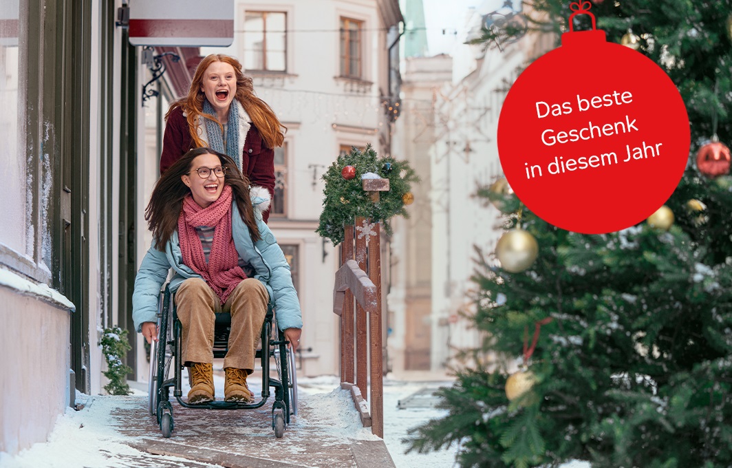 Zwei Freundinnen, eine davon im Rollstuhl, schlendern durch eine schneebedeckte Stadt.