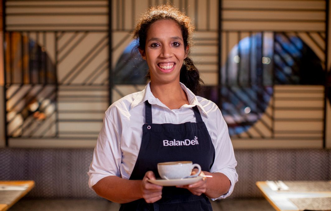 Projekt der Woche "BalanDeli" - Eine junge Frau trägt eine Tasse mit Milchkaffee.