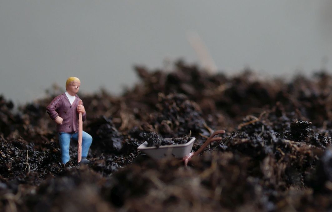 Eine männliche Spielfigur in Arbeitskleidung steht mit Spaten und Schubkarre inmitten von Dreck und Schlamm.