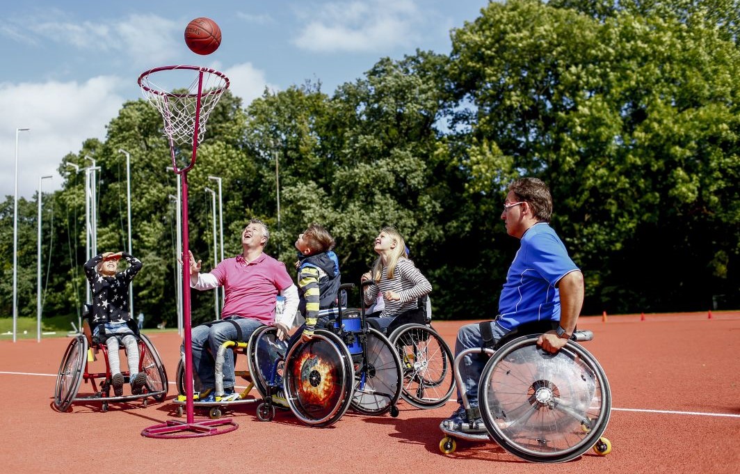 Eine Gruppe Jugendlicher trainiert auf dem Sportplatz Rollstuhl-Basketball.