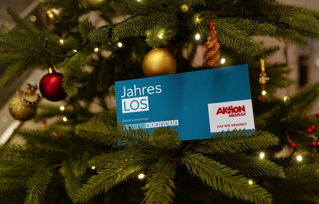 Ein Jahreslos liegt auf einem Zweig eines festlich geschmückten Weihnachtsbaums.