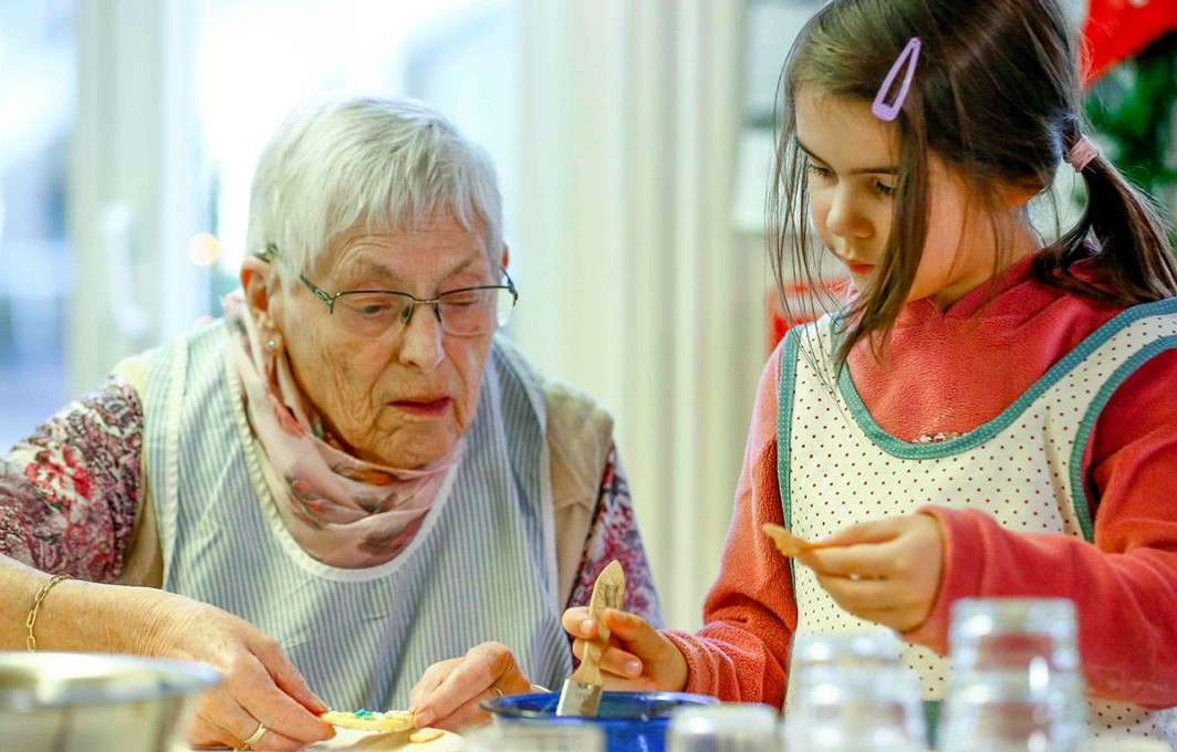 Eine Seniorin und ein Mädchen verzieren gemeinsam Weihnachtsplätzchen.