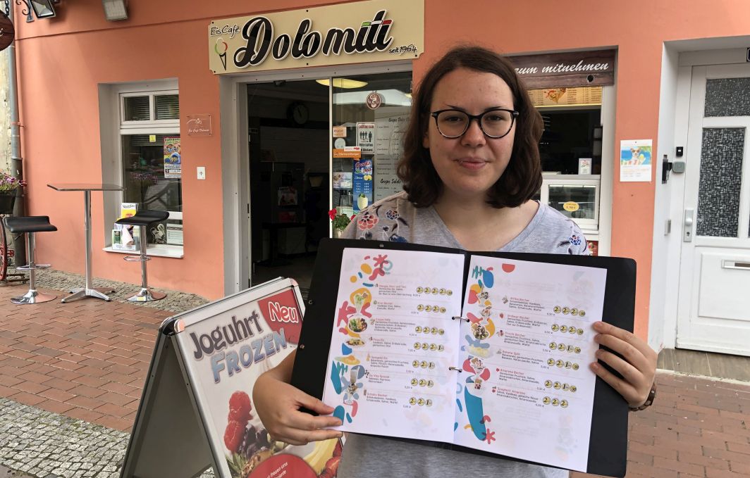 Die Mitarbeiter*innen des EiscafÃ©s posieren vor der Tür. Manche haben eine Eiswaffel in der Hand.