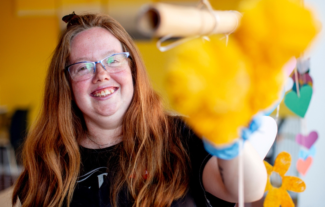 Eine junge Frau mit Brille macht gut gelaunt mit einem knallgelben Staubwedel sauber.
