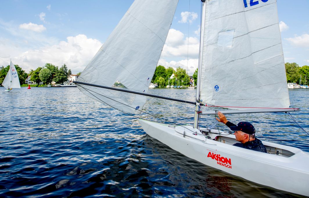 Ein Mann sitzt in einem Segelboot auf einem blauen See. Auf dem Boot ist die Aufschrift "Aktion Mensch" zu lesen.